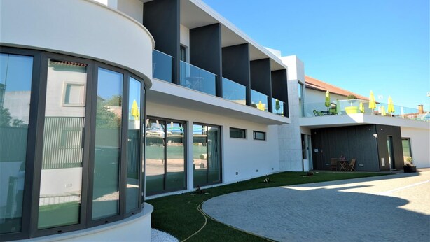 Un bâtiment moderne à deux étages, doté de grandes fenêtres en verre, d’une allée incurvée et d’un petit espace gazonné.