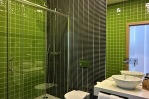 A bathroom with green tiled walls, a glass shower enclosure, a white sink with a bowl, and a wooden door. - Ansiturismo (Ansiao)