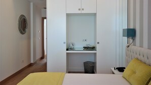 Une chambre à coucher comprenant un lit, une table de chevet, une commode, un bureau avec une chaise, une poubelle, un miroir et une lampe fixée au mur.