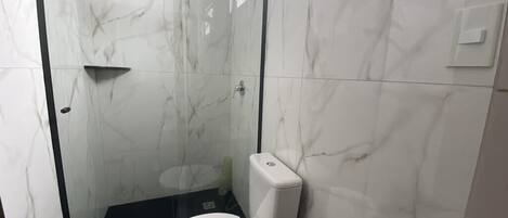A bathroom with a glass-enclosed shower, a white toilet, and marble walls.