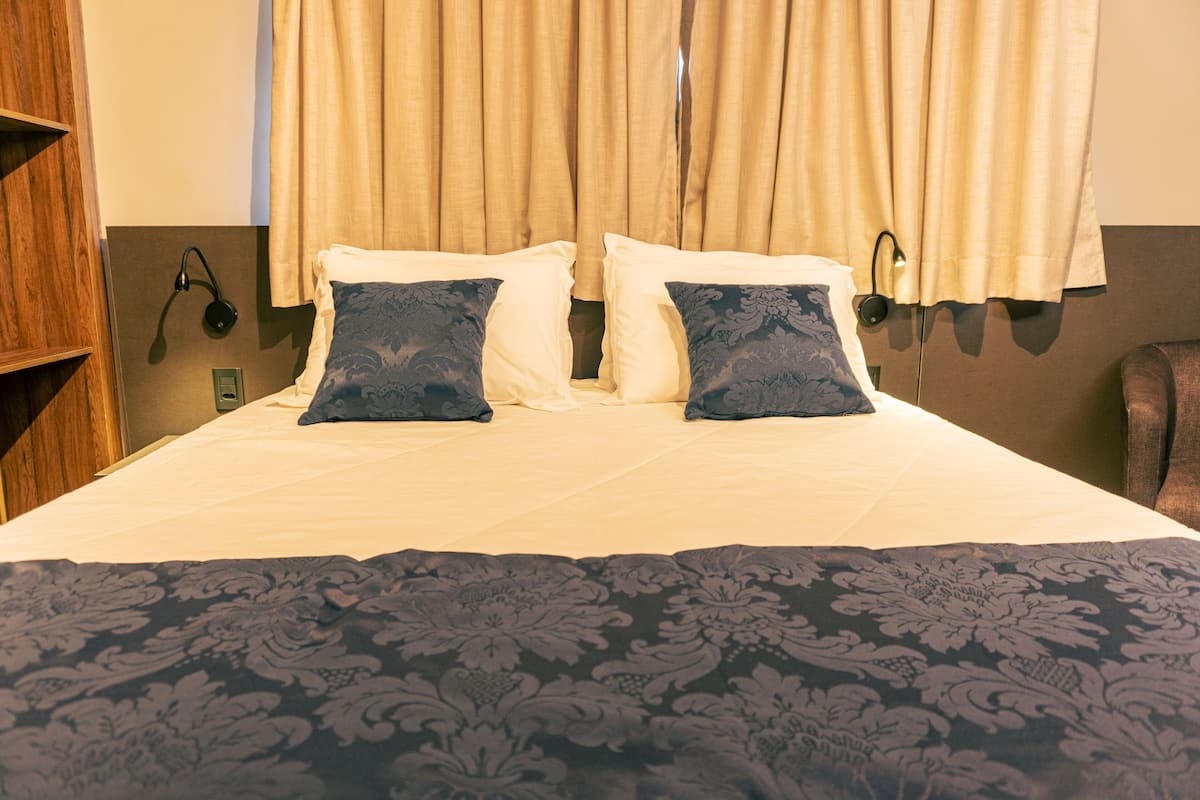 A neatly made bed with a patterned bedspread and two decorative pillows, a wooden headboard, and a wall-mounted light fixture.