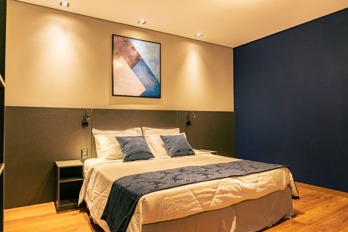 A modern hotel room with a large bed, a nightstand, and a wall-mounted artwork.