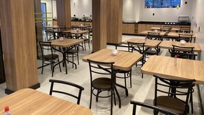 Un comedor moderno con mesas y sillas de madera, una cocina al fondo y un amplio ventanal con vistas.
