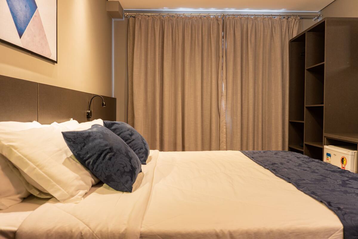 A neatly made bed with pillows, a headboard, a bedside table, and a wardrobe.
