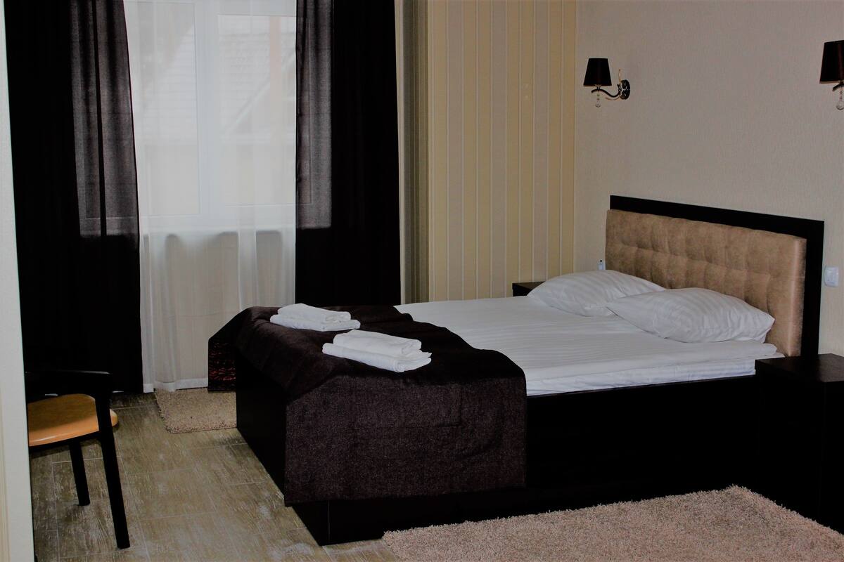 A neatly made bed with white linens, a dark brown headboard, and a small bedside table with a lamp.