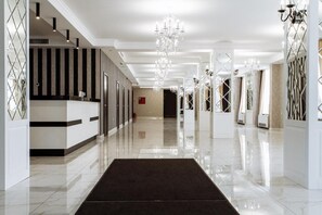 Un hall de hotel espacioso y bien iluminado con un suelo de mármol pulido, una recepción y elegantes candelabros.