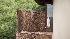 A stone-built outdoor shower area with a waterfall feature, surrounded by lush greenery. - Izingwe Lodge (Vaalwater)