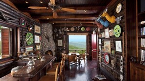 A rustic interior with a stone fireplace, wooden ceiling, and a view of the landscape. - Izingwe Lodge (Vaalwater)