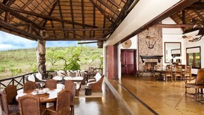 A dining area with a view of the savanna, a stone fireplace, and a dining table with chairs. - Izingwe Lodge (Vaalwater)