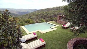 A pool with a view of a mountainous landscape, surrounded by a well-maintained lawn and two lounge chairs. - Izingwe Lodge (Vaalwater)