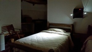 Een kamer in gedempt licht met een enkel bed, een houten stoel en een klein tafeltje.