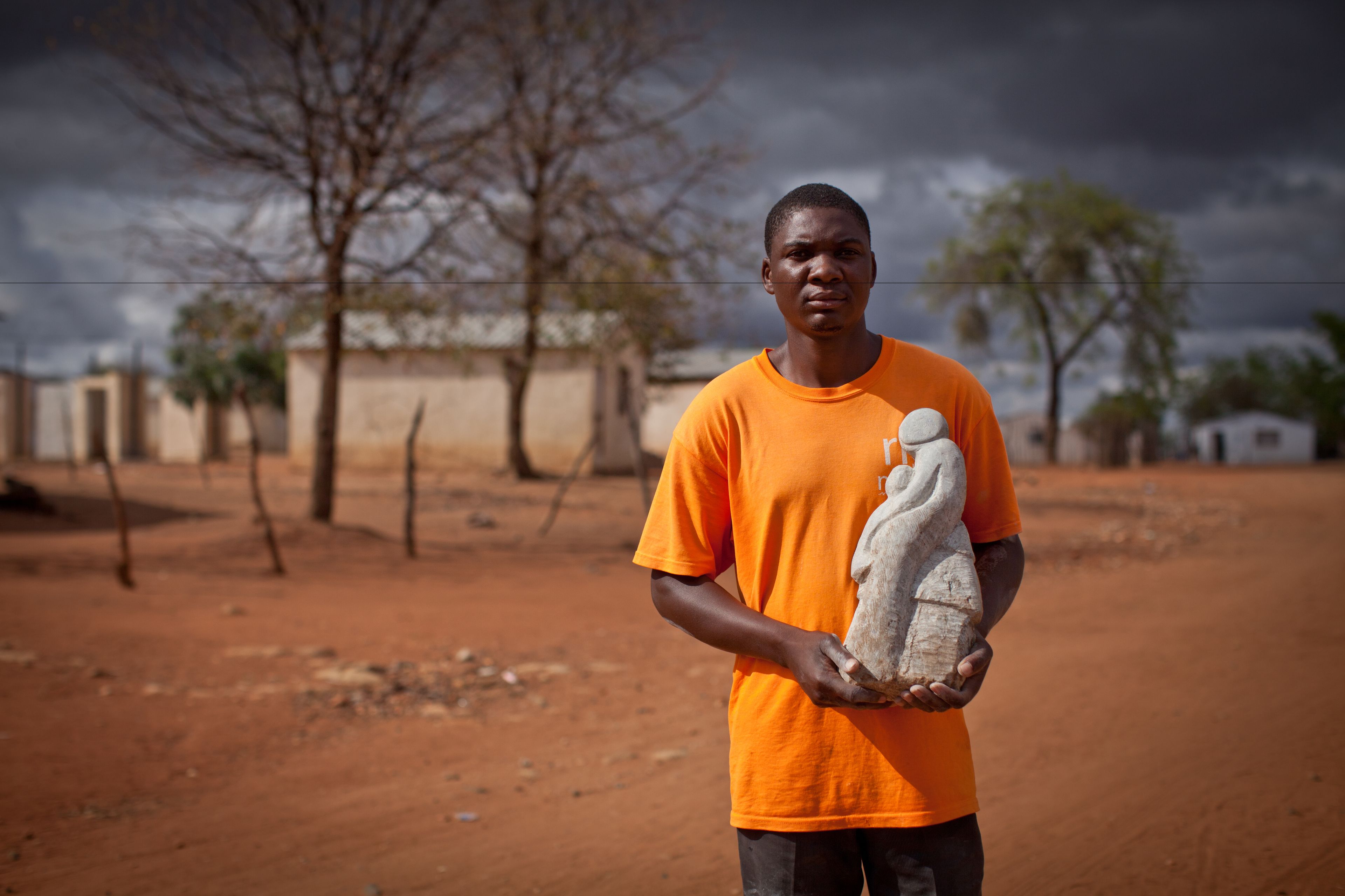 A person in an orange shirt holding a sculpture.