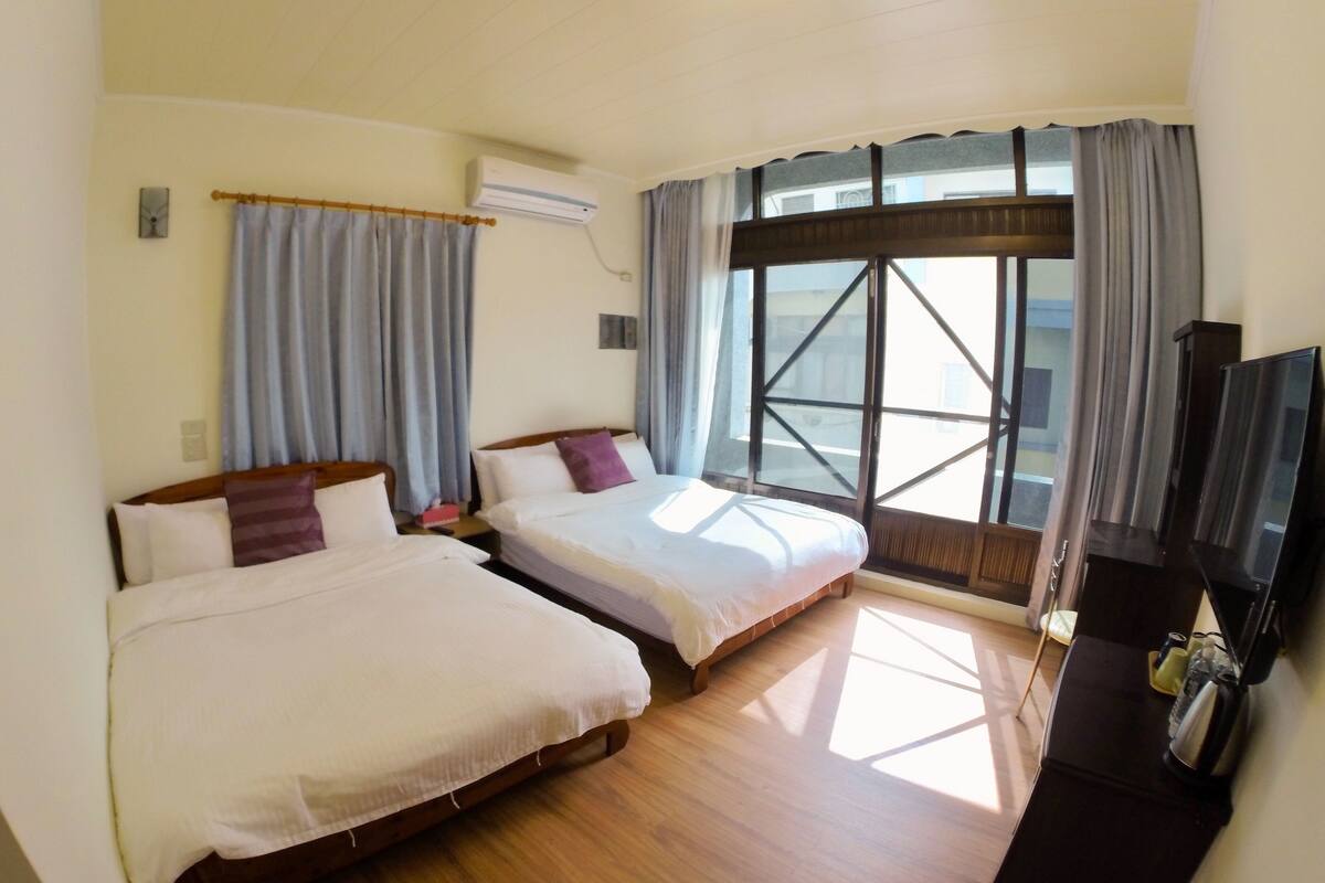 A hotel room with two beds, a TV, and a large window with curtains.