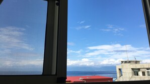 A view through a window with a mesh screen, overlooking a body of water and a building with a red roof. - Good Things (Liuqiu)