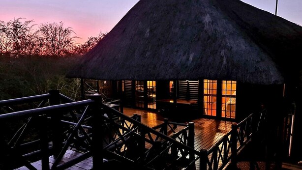Ein Gebäude mit einem Reetdach, Holzgeländern und einer Holzterrasse, vermutlich ein Gästehaus oder eine Lodge.