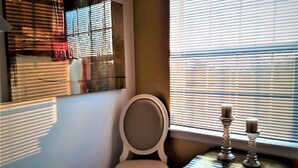A room with a chair, a small table with candlesticks, and a window with blinds.