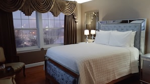 A hotel room with a large bed, a nightstand with a lamp, a chair, and a window with curtains.
