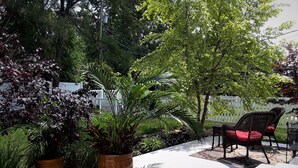 A garden patio with potted plants, a white fence, and outdoor furniture.