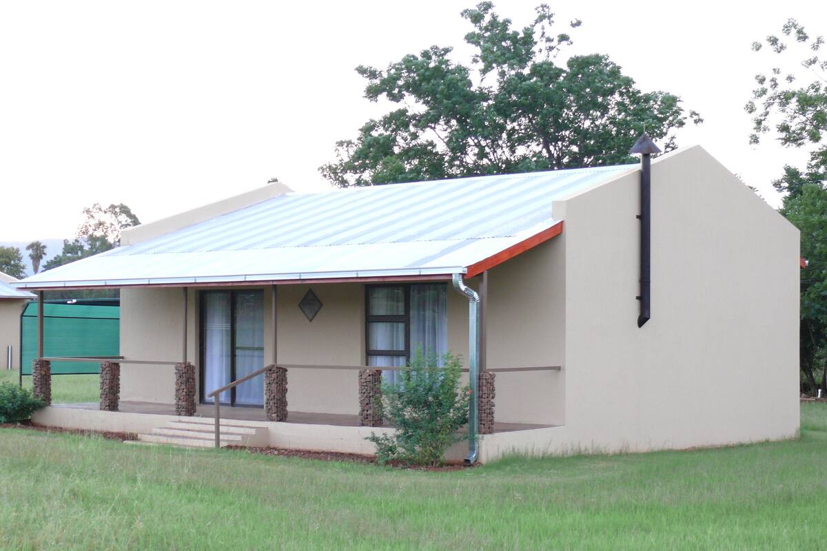 A single-story house with a sloped metal roof, a front porch with stone pillars, and a small front yard.