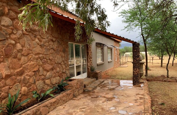 Une maison en pierre avec un porche couvert, un mur en pierre et un petit jardin.