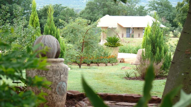 Une maison entourée d’un jardin où poussent différentes espèces de plantes, avec une structure en pierre en premier plan.