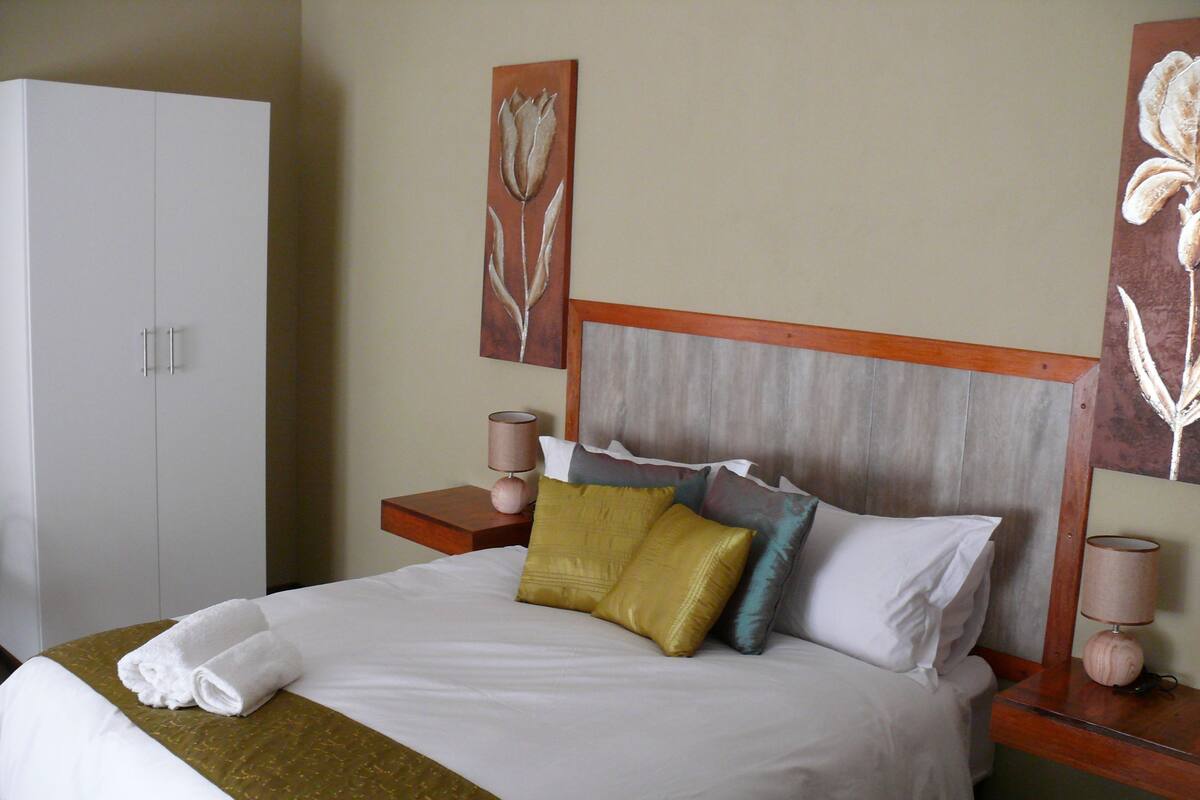 A neatly made bed with a white comforter and a green throw blanket, a wooden headboard, and two bedside tables with lamps.