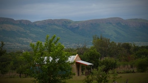 Un petit bâtiment avec un toit rouge, entouré de verdure et avec des montagnes en arrière-plan.