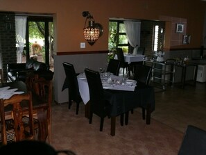 Un espace repas avec des tables disposées pour quatre personnes, des chaises, un luminaire fixé au mur et une vue sur l’extérieur.