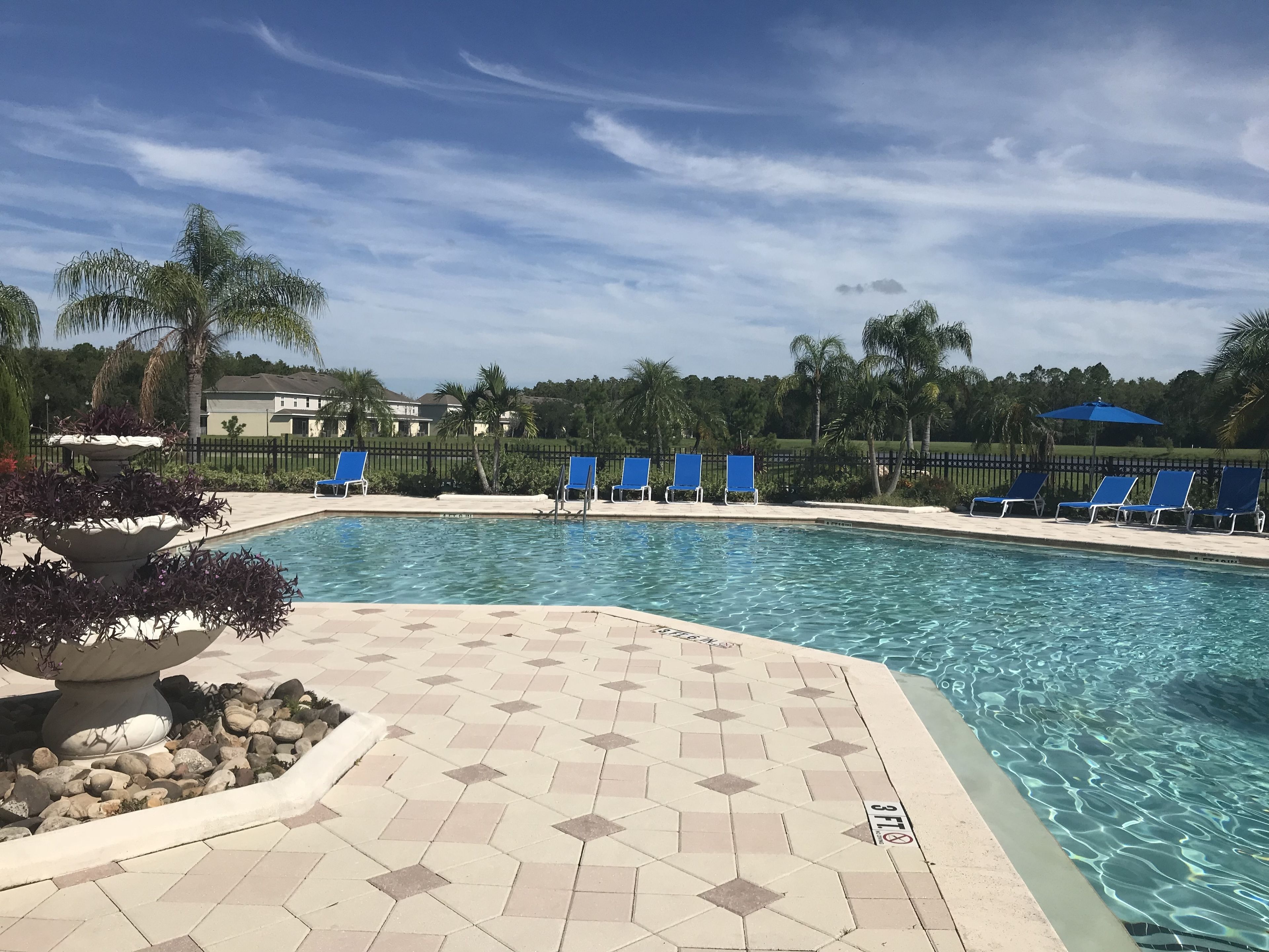 Une piscine entourée de chaises longues bleues, d’une terrasse carrelée et d’un jardinier en pierre agrémenté de plantes.