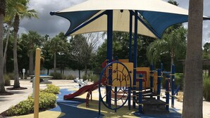 Ein Spielplatz mit einer überdachten Spielanlage, Palmen und einem gepflasterten Weg.