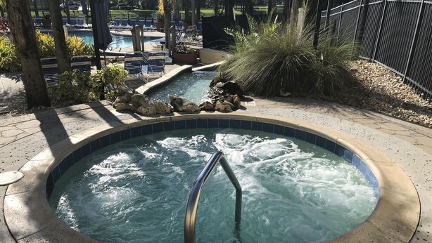 Ein Whirlpool mit Metallleiter, umgeben von Liegestühlen und einem Poolbereich.