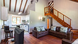 A spacious living area with a wooden staircase, a kitchen with white cabinets, and a dining area with a bar stool. - Kangelani Lodge (Assagay)