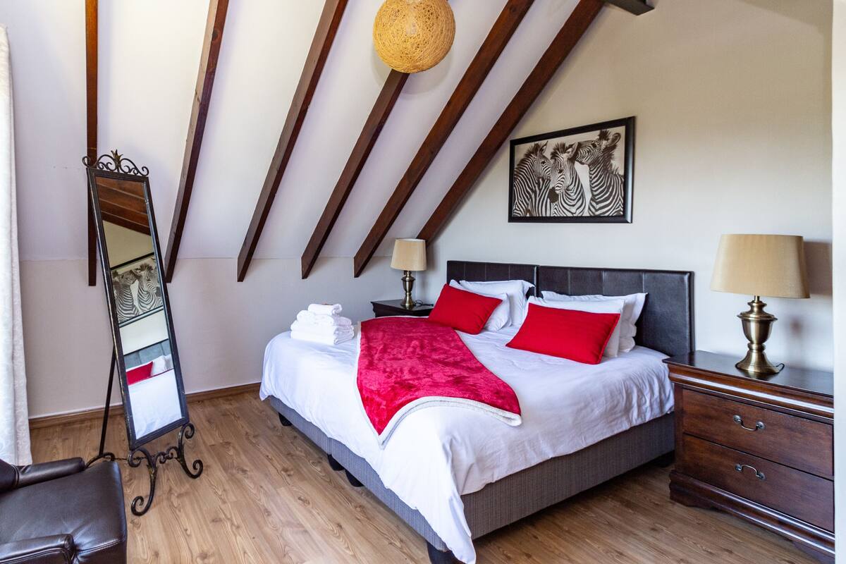 A bedroom with a bed, bedside tables, a mirror, a chair, and a window with curtains.