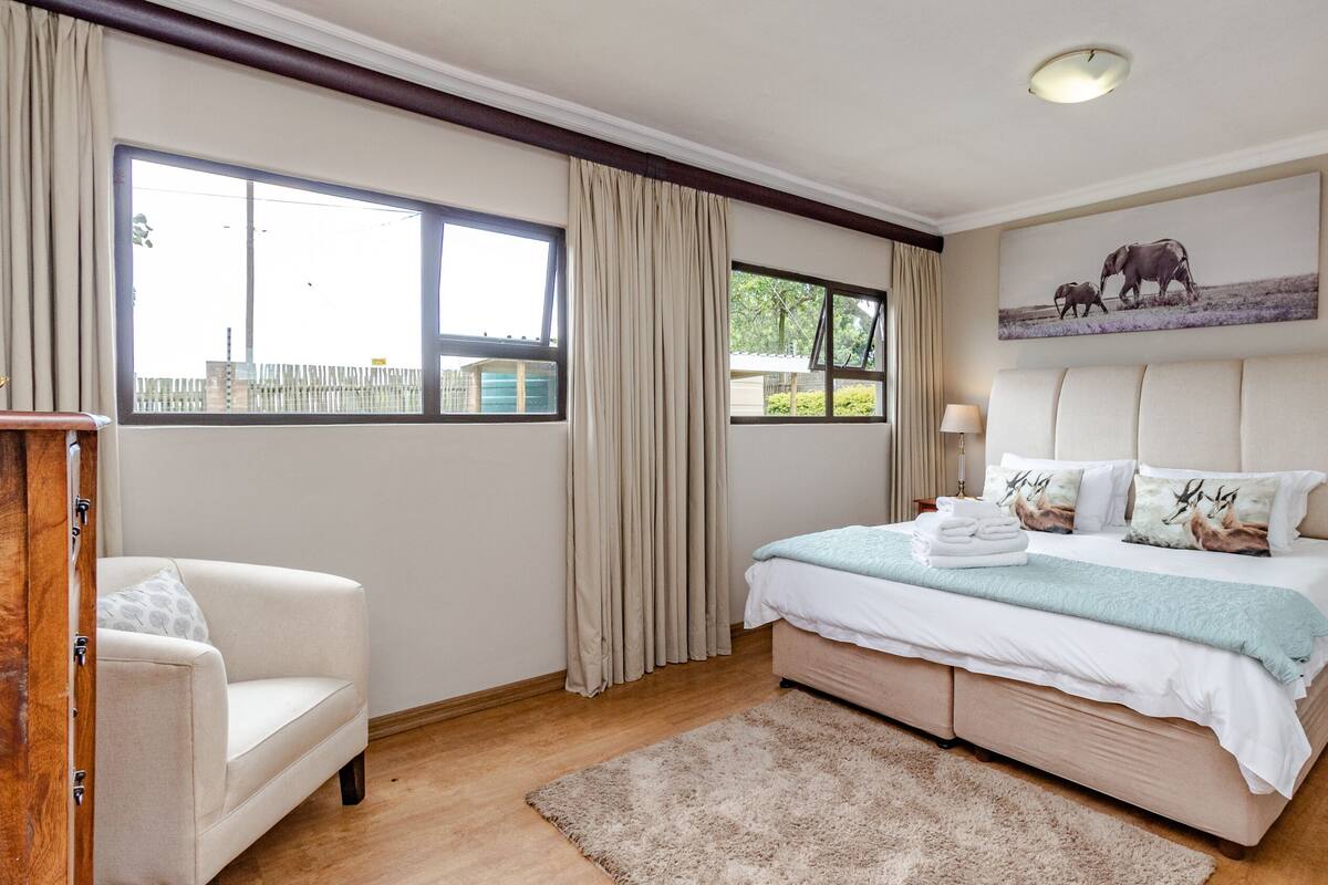 A bedroom with a large bed, a chair, a nightstand, a lamp, and a painting on the wall.