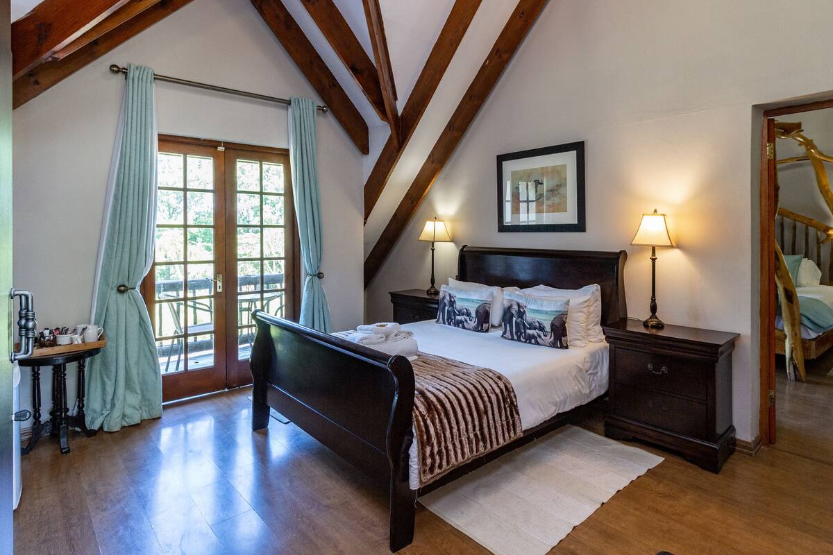 A bedroom with a wooden bed, two bedside tables with lamps, a large mirror, and a view of a wooden staircase.