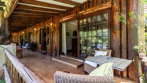 A rustic wooden interior with a long corridor, wicker furniture, and large windows offering a view of greenery. - Kangelani Lodge (Assagay)