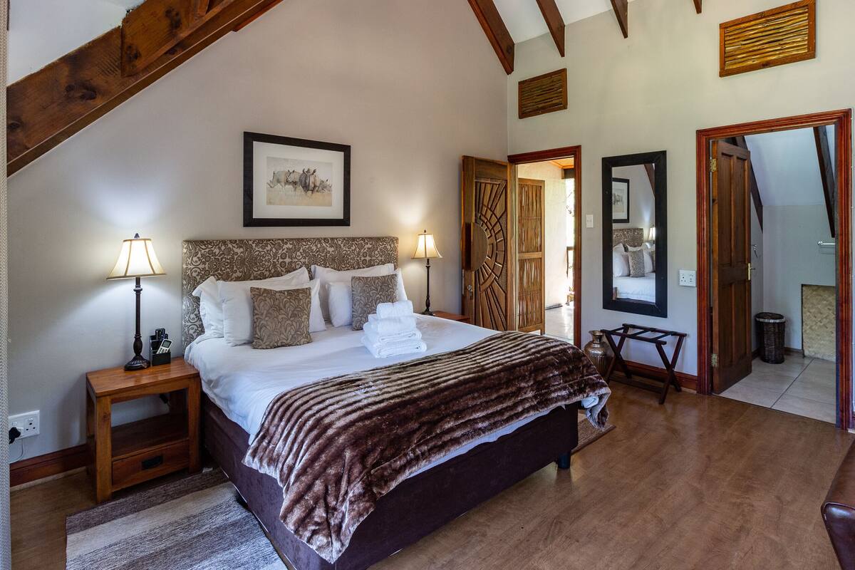 A bedroom with a large bed, bedside lamps, a wooden headboard, a framed picture, and a mirror on the wall.