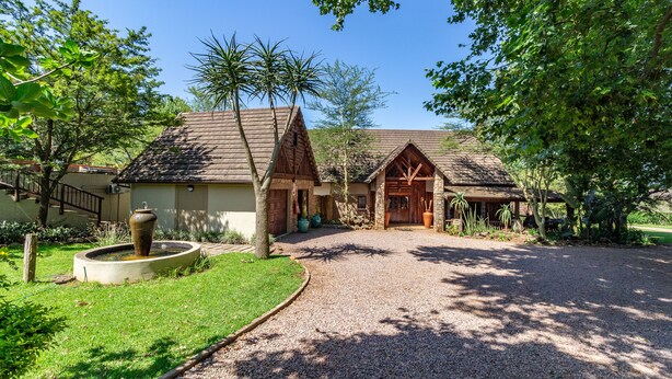 A rustic lodge with a gravel driveway, stone walls, and a wooden entrance. - Kangelani Lodge (Assagay)