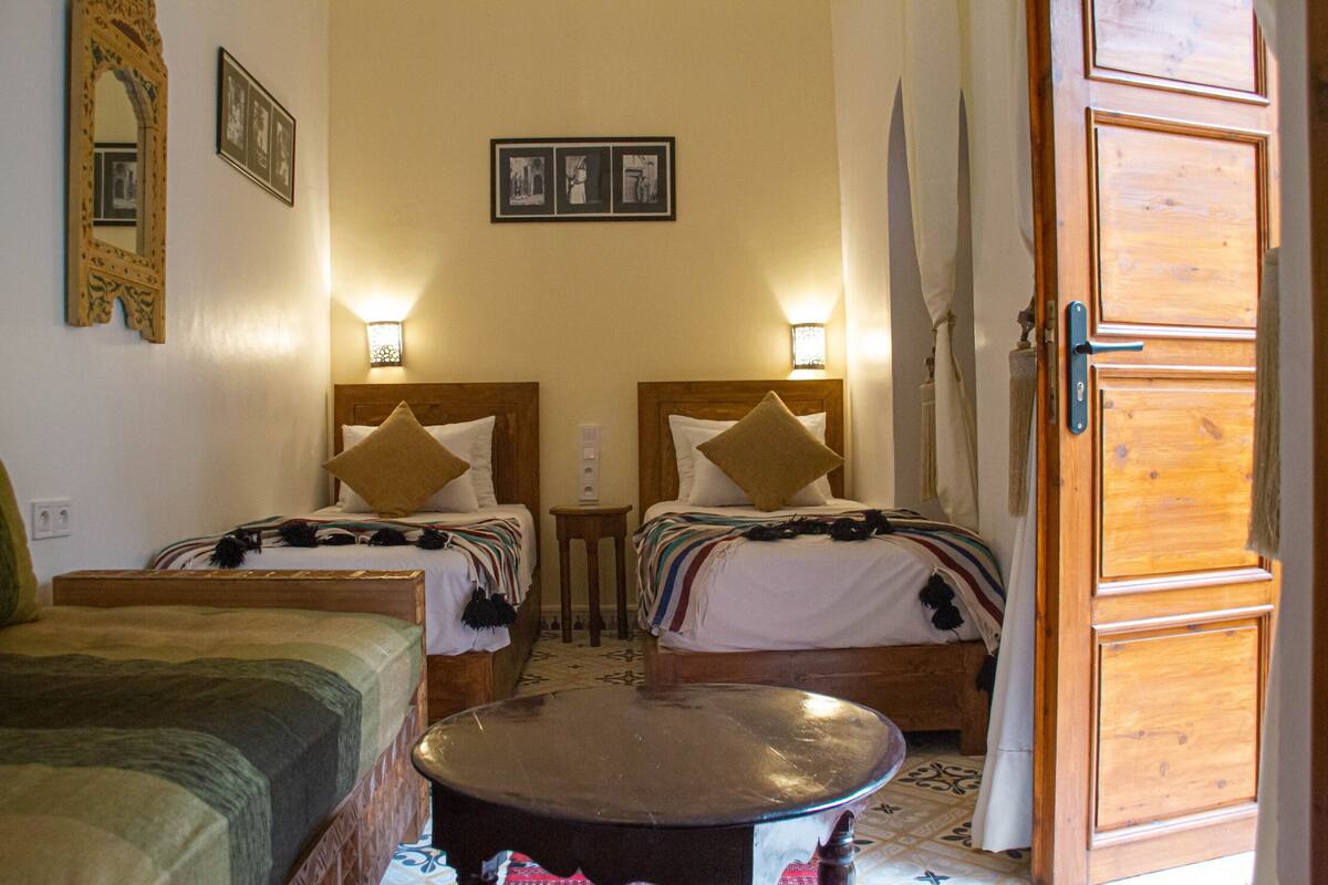 Una habitación con dos camas, una mesa redonda y una puerta de madera.