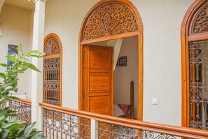 A wooden door with intricate carvings, a wrought iron balcony railing, and a view of a room with a bed and a nightstand. - Riad Dar Tamlil (Marrakech)