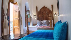 A bedroom with a wooden headboard, a bed with blue and white bedding, and a small table with a mirror. - Riad Dar Tamlil (Marrakech)