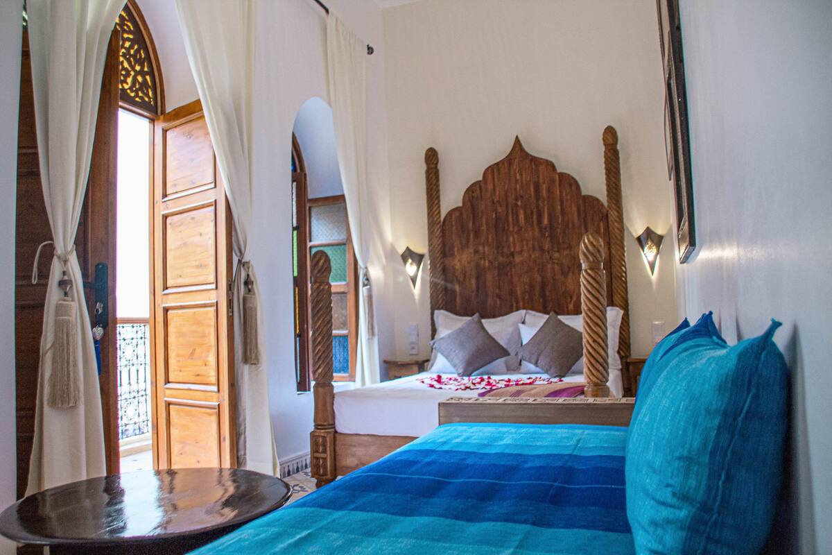Un dormitorio con cabecera de madera, cama con ropa de cama azul y blanca y una pequeña mesa con espejo.