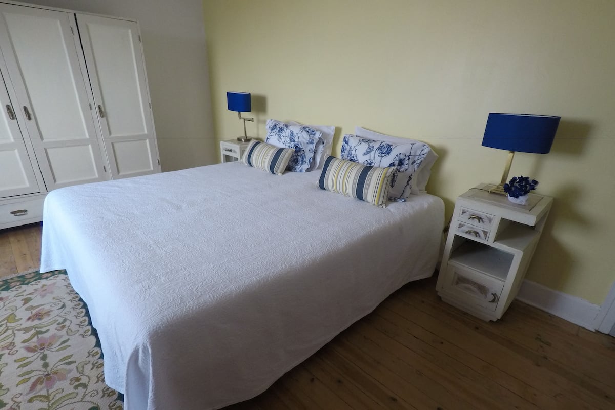 A neatly made bed with a white bedspread, two matching pillows, and two bedside tables with lamps.