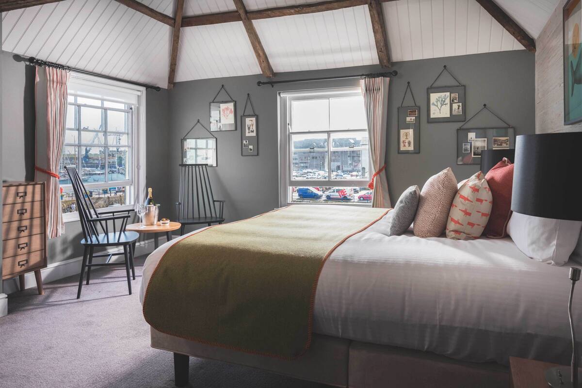Un dormitorio con una cama grande, vistas de la ciudad a través de una ventana y una silla junto a la ventana.