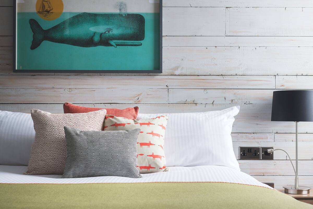 Ein Bett mit gemusterten Kissen, ein gerahmtes Kunstwerk mit einem Walmotiv und eine Nachttischlampe.