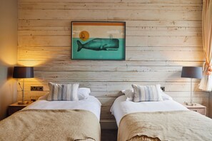 A room with two beds, a wooden wall, a framed picture of a whale, and lamps on either side. - Chainlocker (Falmouth)