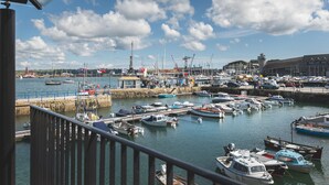 A marina with various boats docked, a crane, and a lighthouse in the background. - Chainlocker (Falmouth)