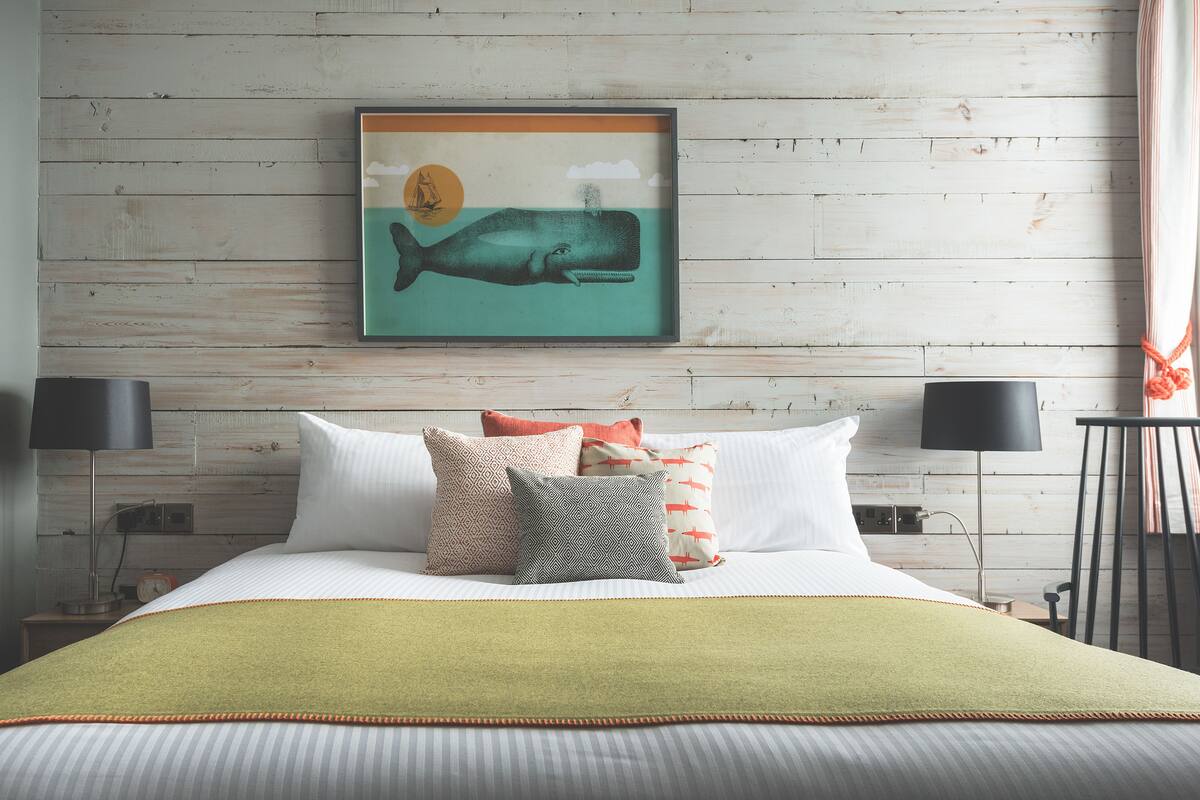 Ein ordentlich gemachtes Bett mit grüner Tagesdecke, einem gerahmten Wal-Kunstwerk an der Wand und einem Holz-Kopfteil.