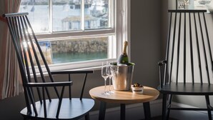 A room with a view of a harbor, a wooden table with a bottle of champagne and two glasses, and two black chairs. - Chainlocker (Falmouth)