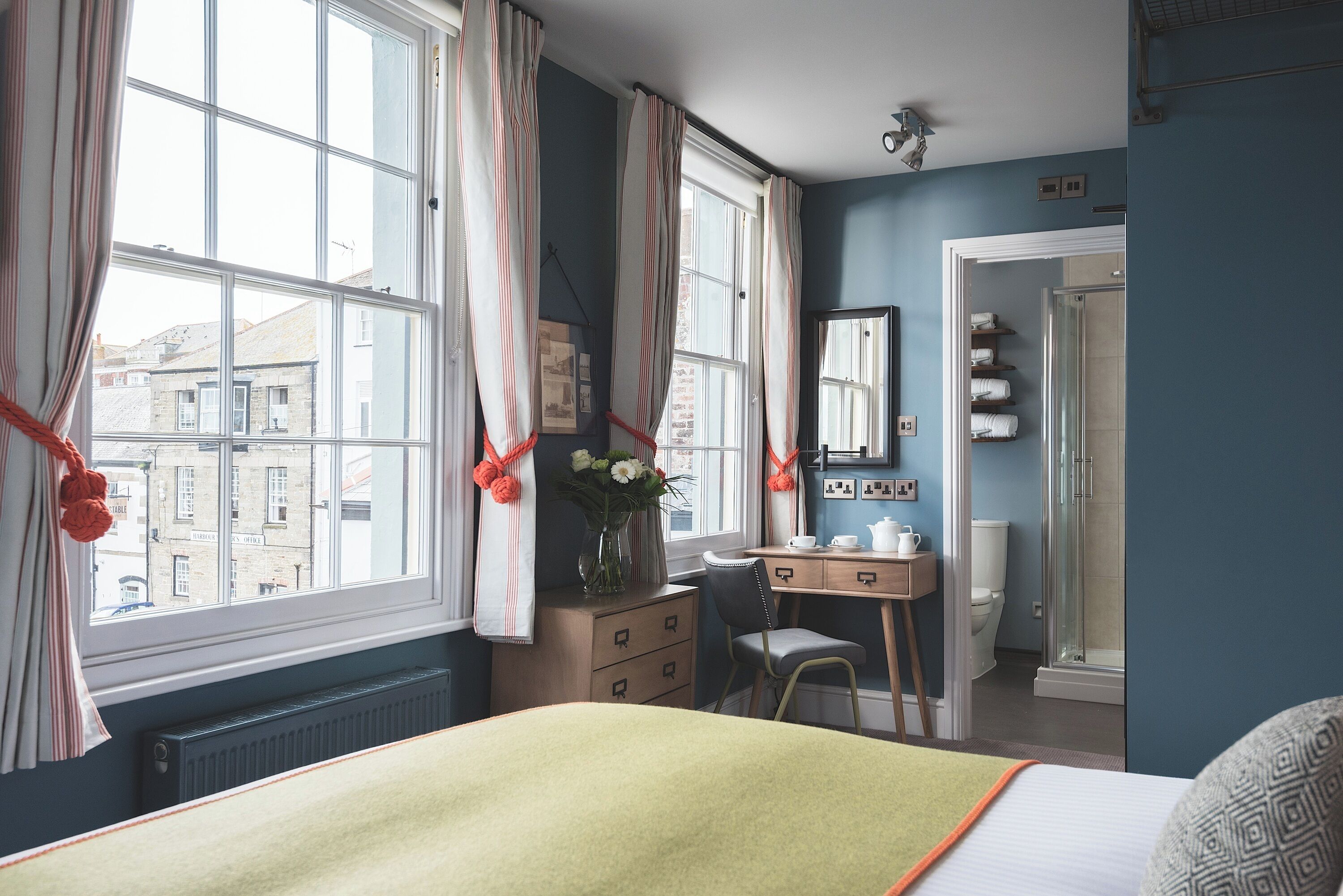 Een slaapkamer met een bed, een bureau, een stoel, een radiator en een raam met gordijnen.